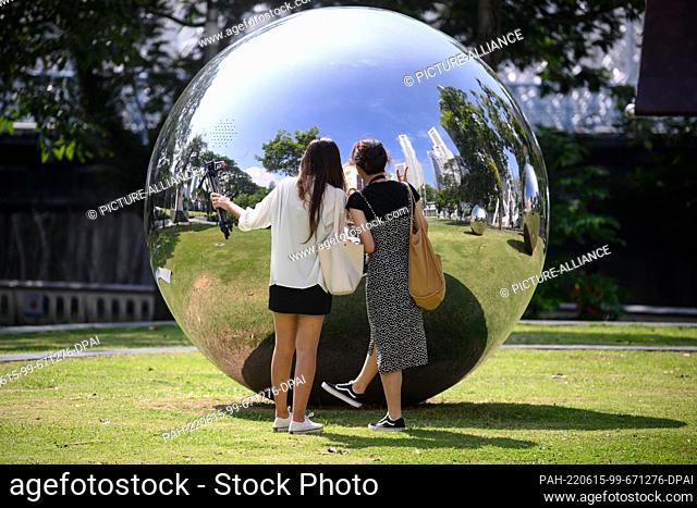 15 June 2022, Singapore, Singapur: Two young women look at each other in a reflecting metal sphere in front of the Asian Civilisations Museum in downtown...