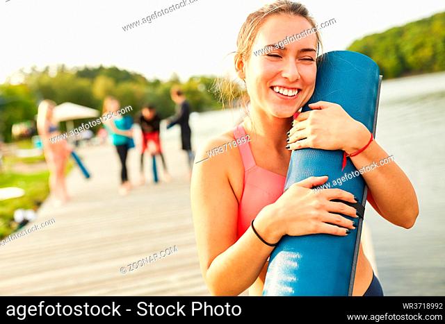 Glückliche junge Frau mit Yogamatte nach dem Fitness Kurs in der Natur am Seeufer