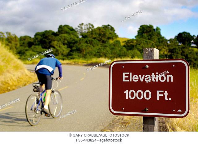 Bicycle rider going uphill on road past elevation marker sign, Mount Diablo State Park, California