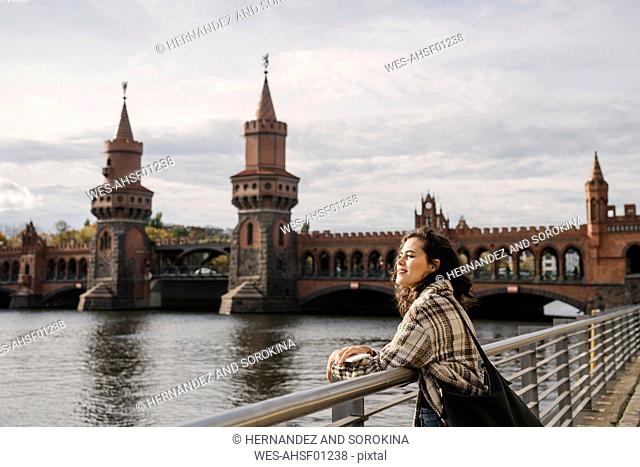 Smiling woman with smartphone in the city at Oberbaum Bridge, Berlin, Germany