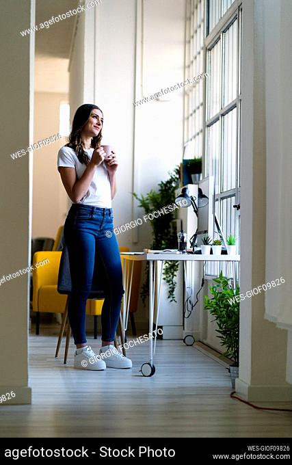 Businesswoman with coffee cup looking away while standing at office