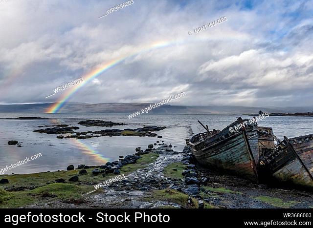 Rainbow and beached old wooden fishing boats on shore at Salen