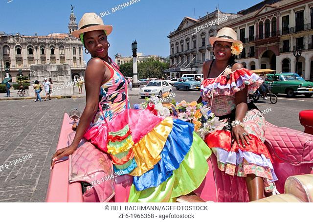 Havana Cuba local women with flowers at Capital in pink Classic Ford auto and hats smiling for tourists
