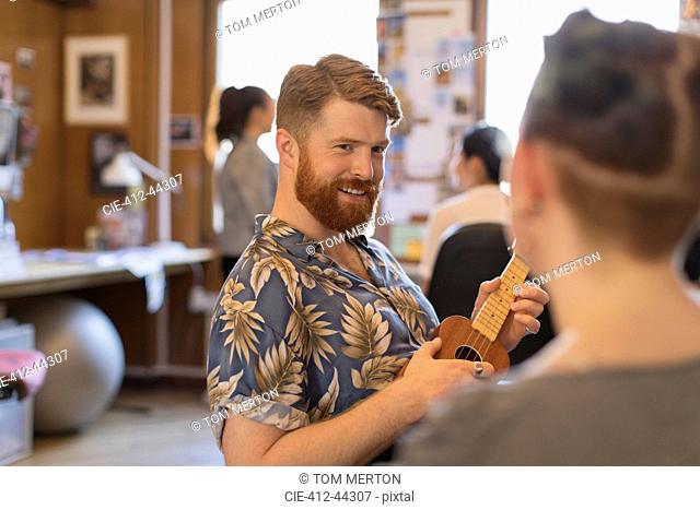 Smiling creative businessman playing ukulele in office