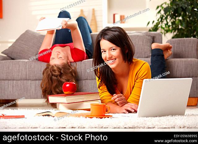 Happy students studying at home in living room with books and laptop, looking at camera smiling
