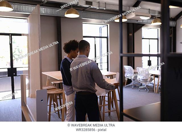 Rear view of young Mixed-race business people discussing over blue print holding by the man standing in modern office