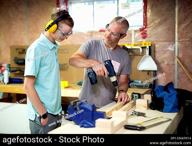 Young man doing woodworking in his basement while his father looks on; Edmonton, Alberta, Canada