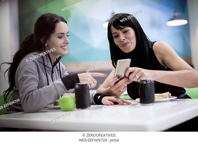 Woman showing cell phone to colleague in office canteen