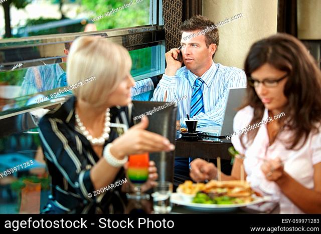 Young women sitting at table in cafe, eating sandwich and drinking cocktail, talking