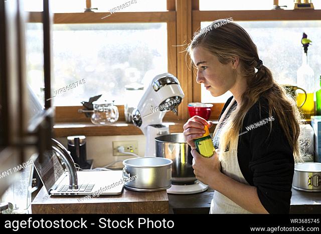 Teenage girl in a kitchen following a baking recipe on a laptop