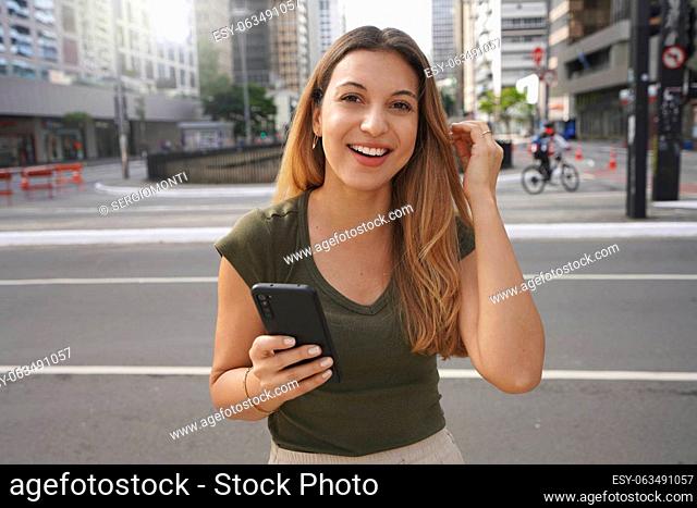 Authentic people outdoors. Self-confident girl with phone looking at camera in empty metropolis in the morning on summer
