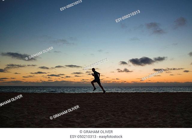 A side-view shot of a caucasian mid-adult man jogging across the beach in Perth, Australia. The sun is setting behind him