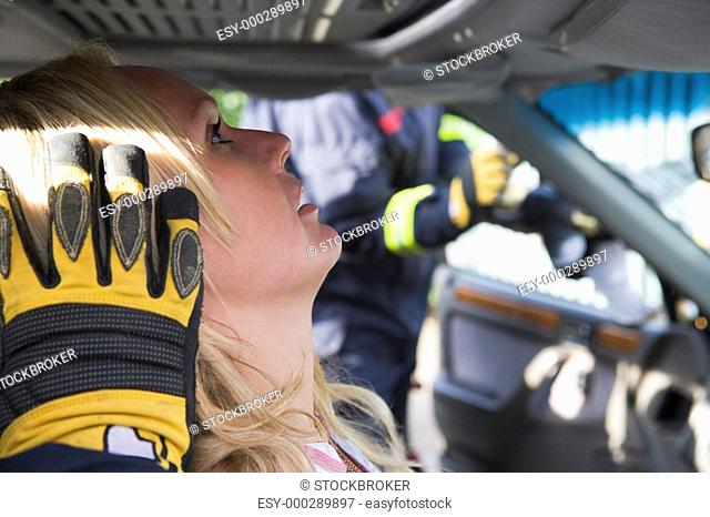 Injured woman in car with firefighter in background cutting out windshield selective focus