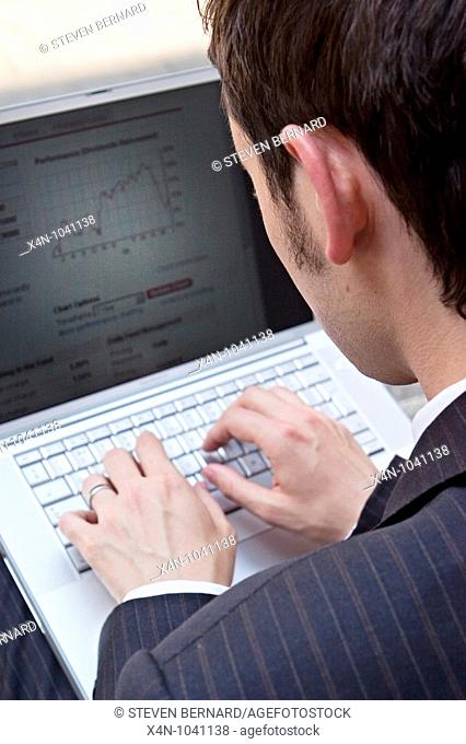 Young businessman looks at financial data on his laptop in the City of London, UK