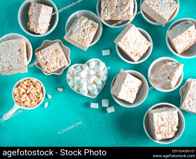 Homemade square bars of Marshmallow and crispy rice and ingredients on azure blue background. American dessert with marshmallow and crispy rice