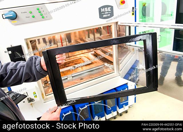 PRODUCTION - 24 February 2022, Schleswig-Holstein, Neumünster: An employee holds a previously printed frame for screens for an ICE in front of a 3D printer at...