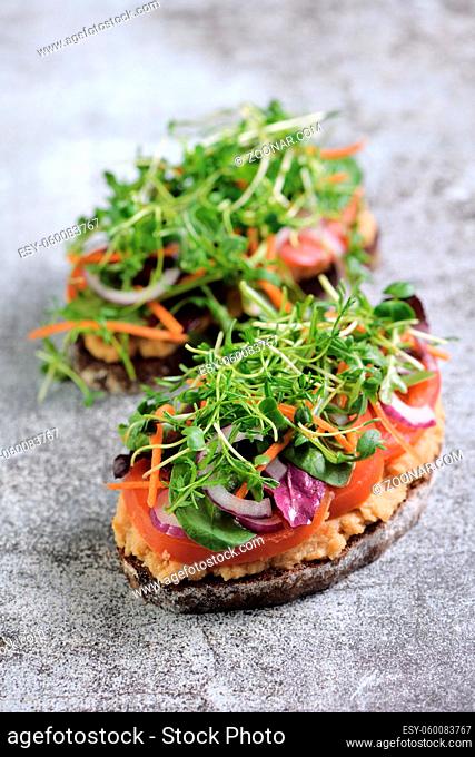 Sandwich toasted rustic bread with chickpea hummus, tomato slices, mix of lettuce and microgreens. Vegetarian breakfast