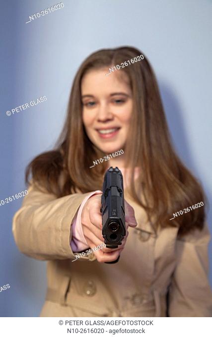 Young woman, wearing a trench coat, holding a gun