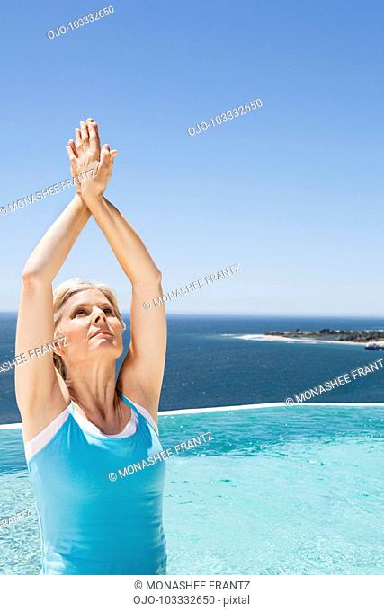 Woman stretching arms overhead at poolside overlooking ocean