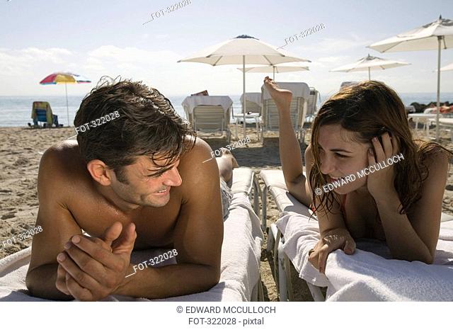 Young couple lying on deck chairs at beach