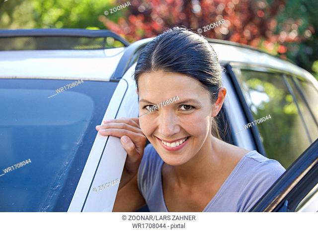 young woman leans against her car