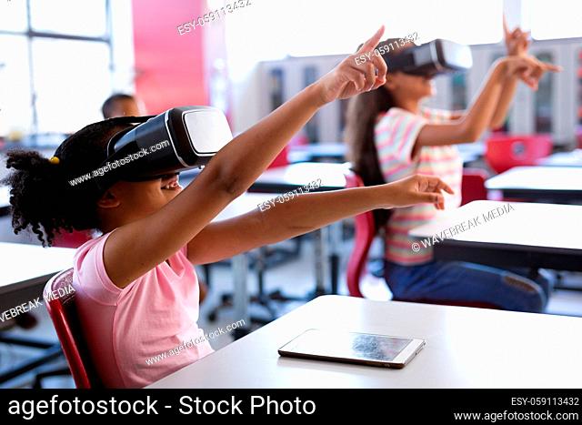 African american girl wearing vr headset gesturing while sitting on her desk in the class at school