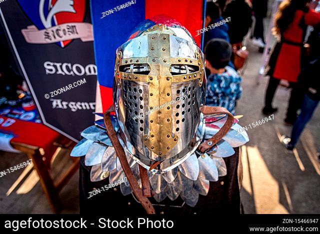 Shiny silver medieval iron knight helmet with a golden cross, full of scratches due to battles