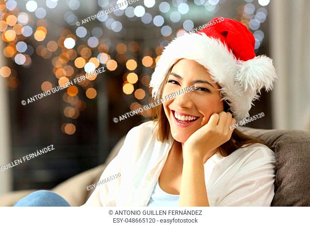 Happy woman looking at you on chritmas sitting on a couch in the living room at home
