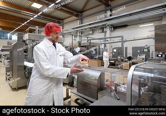 18 December 2023, Saxony, Riesa: Michael Kretschmer (CDU), Minister President of Saxony, holds a pack of Chinese noodles while wearing a hairnet and smock at...