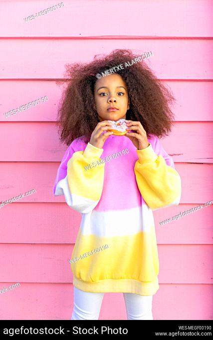 Girl with doughnut standing in front of pink wall