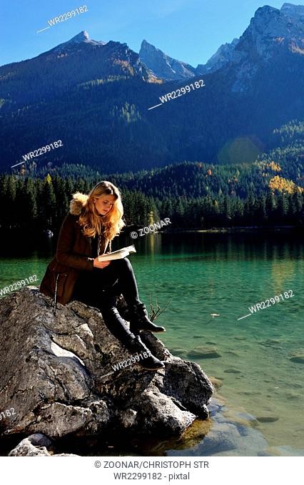 Young woman reading at a mountain lake