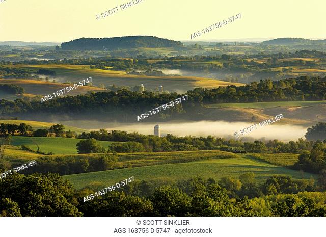 Agriculture - Dairy land at sunrise showing cornfields, alfalfa fields, dairies, silos and fog in low lying areas / S.W. WI
