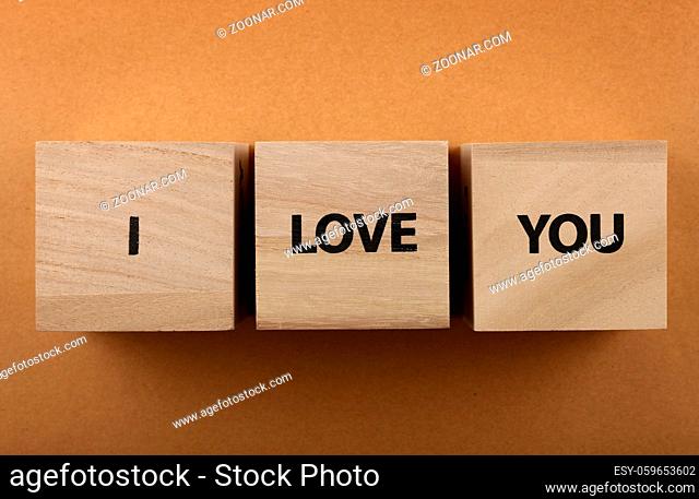 Wooden cube signs with I LOVE YOU words over over background of brown kraft paper with copy space, elevated top view, directly above