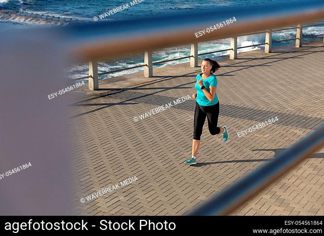 High angle side view of a mature middle aged Caucasian woman working out on a promenade on a sunny day, running