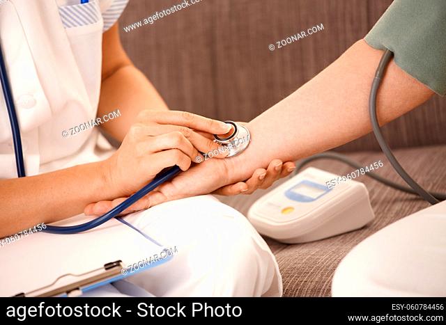 Closeup of nurse using stethoscope on wrist of senior woman