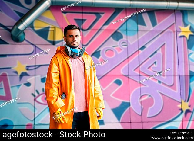 Young graffiti painter standing near the wall with his paintings with copy space. Street art concept