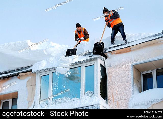 PETROPAVLOVSK CITY, KAMCHATKA PENINSULA, RUSSIA - DEC 27, 2017: Workers with snow shovels carry out winter cleaning of roof of building from snow and ice after...