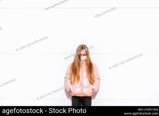 Girl wearing protective face mask standing against wall during COVID-19