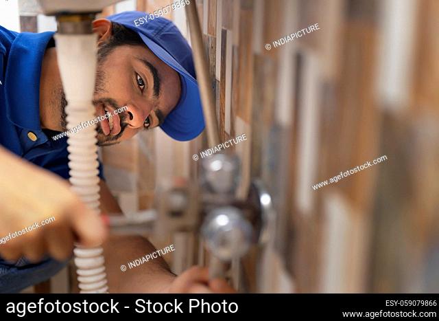 A PLUMBER LEANING DOWN AND FIXING PIPE