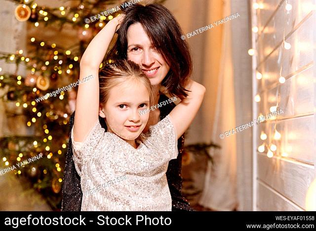 Daughter with arm around smiling mother at home during Christmas