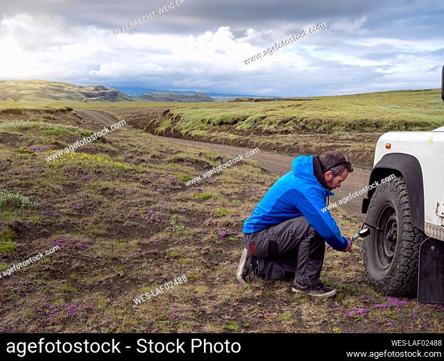 Male tourist kneeling while examining tire pressure through equipment at roadside