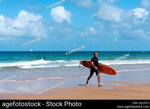 Sables D Or Les Pins, Bretagne / France - 20 August 2019: Middle-aged surfer walking on the beach after a fun surfing session in the waves on the coast of...