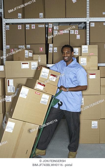 Male African warehouse worker using hand truck