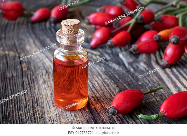 A bottle of rose hip seed oil with fresh berries on a rustic background