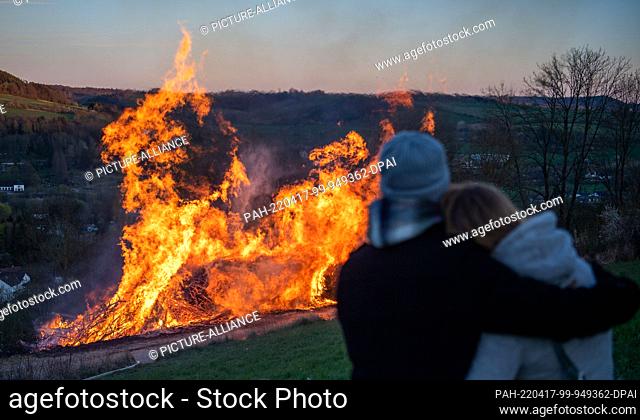 17 April 2022, North Rhine-Westphalia, Lügde: A couple stands by an Easter fire. When it is dark the straw in the wheels is lit and the wheels are pushed down...