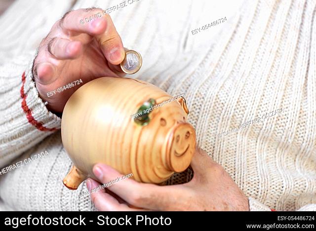 Savings, money, annuity insurance, retirement and people concept - close up of senior man hand putting coin into piggy bank