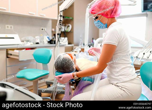Female dentist holds mask, patient in chair, stomatology clinic. Doctor in uniform, medical worker, stomatologist, medicine and health