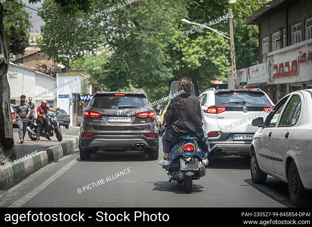 27 May 2023, Iran, Teheran: A woman sits on the back seat of a moped with her hair uncovered; the license plate is not visible