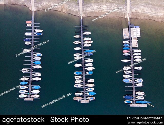12 September 2020, North Rhine-Westphalia, Attendorn-Wamge: Sailing boats are moored at the Bigge lake at a sailing port with jetties