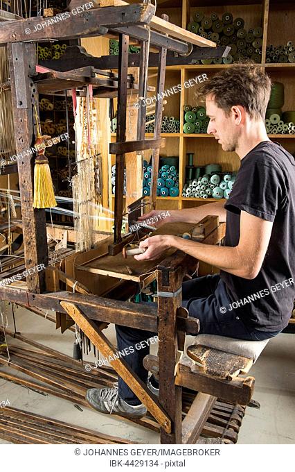 Passementerie maker, man sitting at handloom, weaving crepine or woven border, shelf with thread reels behind, Munich, Bavaria, Germany